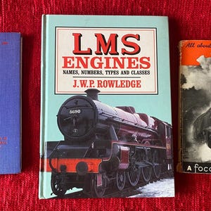 May include: Three vintage railway books on a red background. Titles include "British Rail", "LMS Engines", and "All about Photographing Trains". The "LMS Engines" book shows a black steam train. The "British Rail" book is blue.