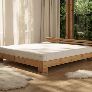 May include: A light-colored wooden bed frame with a mattress, set in a bright room. The bed has a simple, modern design with a headboard. The room features large windows and sheer curtains, with a fluffy rug on the floor.