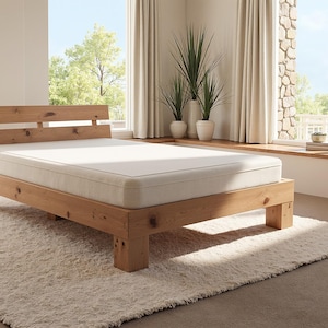 以下が含まれることがあります： 白いマットレスが付いた木製ベッドフレーム。ベッドは大きな窓と床の敷物がある部屋にあります。