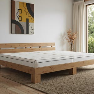 May include: A light-colored wooden bed frame with a mattress. The bed has a headboard with horizontal slats. The mattress is white with a black trim. The bed sits on a neutral-colored rug. An abstract painting hangs on the wall.