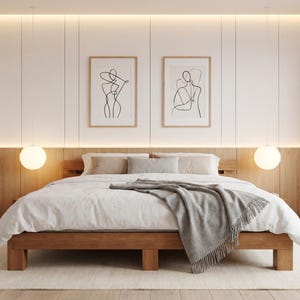 May include: A modern bedroom featuring a wooden bed frame with a white comforter and a gray throw blanket. Two framed line art prints hang above the bed. Two spherical pendant lights illuminate the space, creating a warm ambiance.