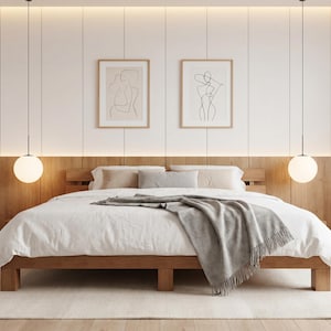 Puede incluir: Un dormitorio moderno con una estructura de cama de madera, ropa de cama blanca y una manta gris. Dos grabados enmarcados de arte lineal cuelgan sobre la cama. Dos lámparas colgantes con pantallas esféricas cuelgan del techo.
