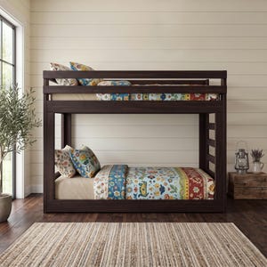 Puede incluir: Una litera de madera de color marrón oscuro con un marco rectangular y listones horizontales. Ambas camas cuentan con colchones claros y ropa de cama estampada con motivos florales y geométricos en tonos azules, rojos y amarillos.