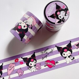 May include: Purple and white striped washi tape featuring Kuromi, a black cat character with pink bows and a skull on her head. The tape has a pink heart with the text "Chaotic but charming" and the text "Kuromi is always in style!" The tape is rolled up and the end of the roll has a pink and purple sticker with the text "Kuromi" and a picture of Kuromi.