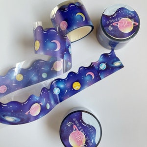 May include: Three rolls of washi tape with a galaxy and planet design. The tape is clear and has a scalloped edge. The text on the tape reads "欧派流心不酱装饰胶带 星川入梦".
