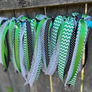 Può includere: Una collezione di nastri verdi, neri e bianchi legati insieme. I nastri sono realizzati con materiali diversi, tra cui pizzo, pois e motivi a chevron.