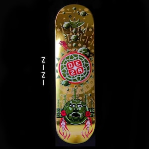 May include: Gold skateboard deck with a green and red design. The design features a circular pattern with the letters "DEZA" in the center. There is a green face with a mouth and eyes in the lower half of the deck.