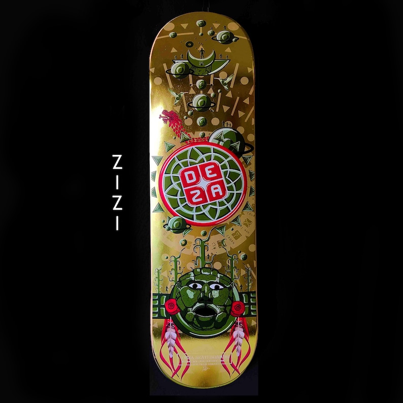 May include: Gold skateboard deck with a green and red design. The design features a circular pattern with the letters "DEZA" in the center. There is a green face with a mouth and eyes in the lower half of the deck.