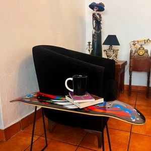 Puede incluir: Un sillón negro con una mesa de skate delante. La mesa tiene un diseño colorido y una taza y libros encima.