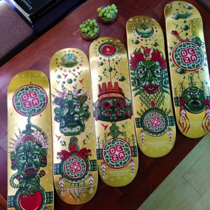 May include: Five colorful skateboard decks with intricate designs featuring green and red mythical creatures, gold accents, and the text "Deza Skateboards".