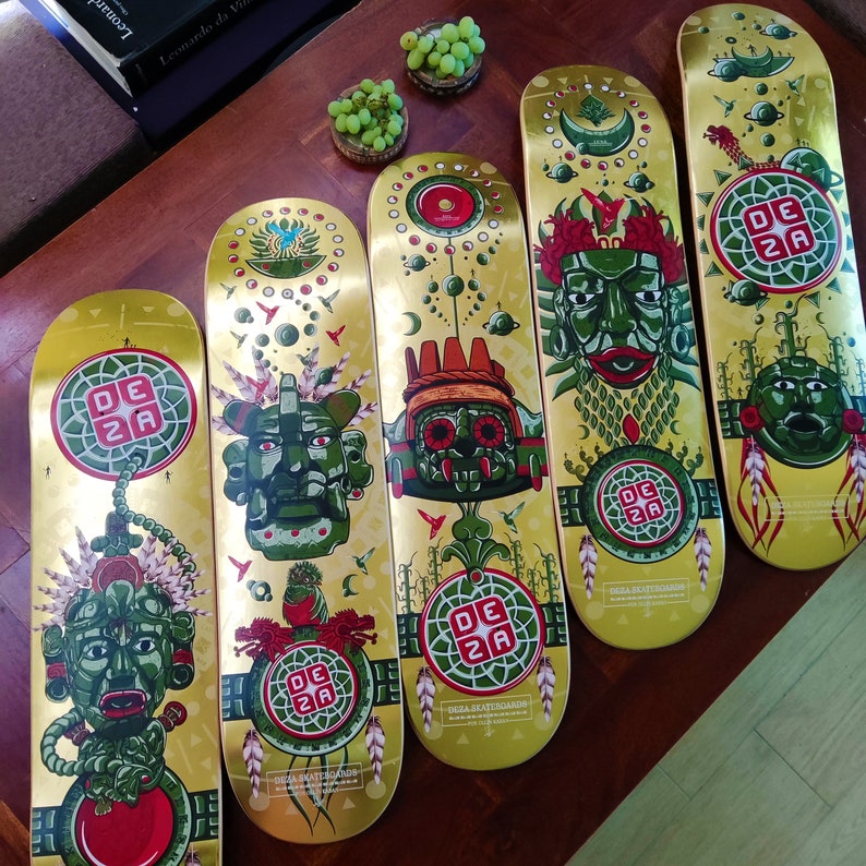 May include: Five colorful skateboard decks with intricate designs featuring green and red mythical creatures, gold accents, and the text "Deza Skateboards".