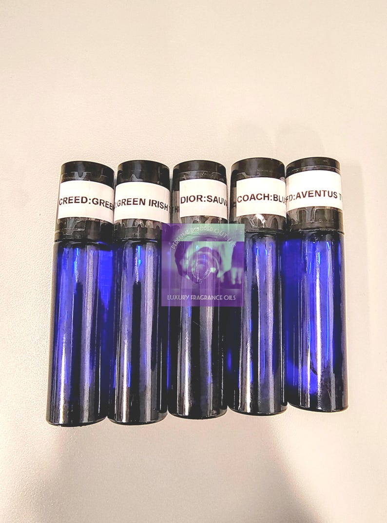 May include: Five blue glass roll-on bottles with black caps are displayed. The labels read "CREED: GREE", "GREEN IRISH", "DIOR: SAU", "COACH: BLU", and "AVENTUS T". The bottles are arranged vertically, suggesting a fragrance or essential oil product.