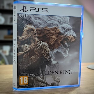 Könnte beinhalten: Ein blaues PlayStation 5-Spielecase mit weißem Hintergrund. Die Vorderseite des Cases zeigt ein großes Bild eines Löwen mit einer Krone auf dem Kopf und einem Krieger im Vordergrund. Der Titel "ELDEN RING" ist in Schwarz am unteren Rand des Cases aufgedruckt. Das Spiel ist von PEGI mit 16+ bewertet.