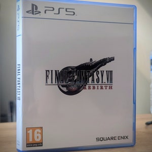 Puede incluir: Una caja de juego de PlayStation 5 blanca con un borde azul. La parte frontal de la caja presenta el logotipo de Final Fantasy VII Rebirth con una imagen en blanco y negro de una nave espacial. La caja también incluye una clasificación 16+ del sistema de clasificación PEGI y el logotipo de Square Enix.