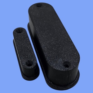 Può includere: Due oggetti neri, rettangolari e strutturati con estremità arrotondate e due fori ciascuno, uno grande e uno piccolo. Gli oggetti sono su uno sfondo azzurro. L'oggetto più grande è lungo circa 10 cm.