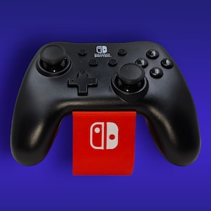 May include: Black Nintendo Switch Pro Controller with a red and white logo. The controller features two analogue sticks, a directional pad, and action buttons. Designed for use with the Nintendo Switch gaming console.
