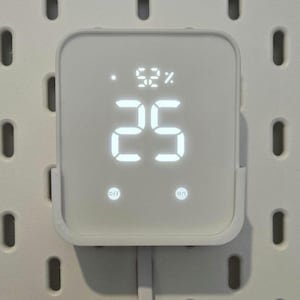 May include: A white digital device displaying the numbers "25" and "52%" in bright white against a white background. The device has "off" and "on" buttons. A white cord extends from the bottom.