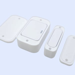 May include: White plastic electrical switches and covers. The image shows two rectangular switches with a button and two covers. The covers have two holes. The switches are on a light blue background.