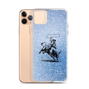 May include: Clear phone case with a blue glitter background and a black and white illustration of a rodeo cowboy riding a bull. The cowboy is holding a lasso. The phone case is made of clear plastic.