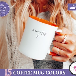 May include: White ceramic mug with an orange interior, featuring the text "married af" and a heart symbol. The mug is held by a person. The image also includes text that says "11 OZ & 15 OZ CERAMIC MUG" and "15 COFFEE MUG COLORS".