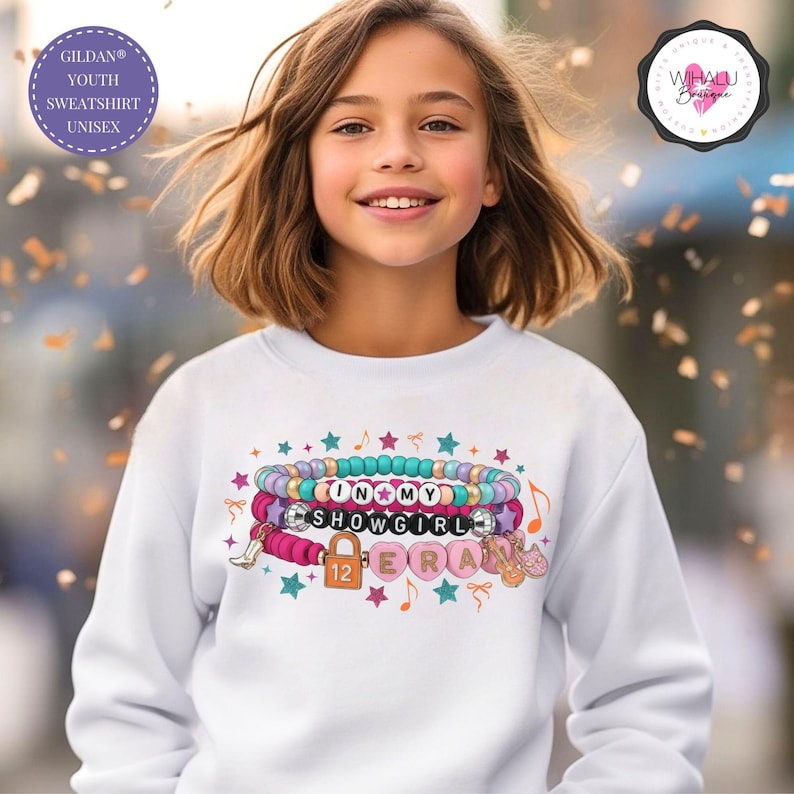 Girl wearing a white Gildan youth sweatshirt with an In My Showgirl Era friendship bracelet design in pink and teal pop culture inspired concert tee beaded bracelet design showgirl era gift for fans of music eras gift idea album ts 12 inspired shirt taylor hoodie, kids taylor hoodie, youth sweatshirt, girls sweatshirt, toddler sweatshirt, youth crewneck, taylor apparel, taylor girls clothes, showgirl hoodie, kids showgirl shirt, youth showgirl tee, girls taylor shirt, showgirl costume