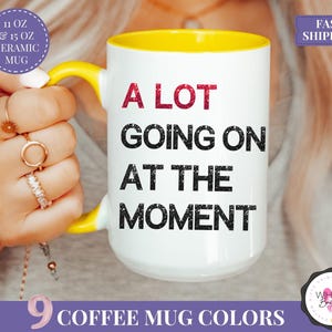 Puede incluir: Taza de cer&aacute;mica blanca con asa e interior amarillos. La taza presenta el texto "A LOT GOING ON AT THE MOMENT" en negro y rojo. La taza est&aacute; disponible en 9 colores y es una taza de cer&aacute;mica de 325 ml o 444 ml.