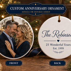 May include: A round white ceramic anniversary ornament featuring a photo of a couple on the front and dark blue text on the back that reads The Robinsons, 25 Wonderful Years, Est. 1999, with a small heart and leaf graphic accents.