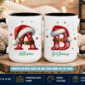 May include: Two white ceramic mugs with black handles and rims. Each mug features a large red letter, 'A' and 'B', decorated with a Santa hat, a brown belt with a gold buckle, and white snowflakes. The names 'Allison' and 'Bethany' are printed below.