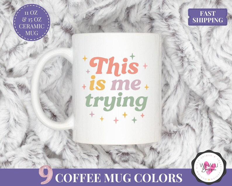 May include: White ceramic mug with the text "This is me trying" in a retro font. The mug is available in 11 oz and 15 oz sizes. The image also includes text indicating "9 Coffee Mug Colours" and "Fast Shipping".