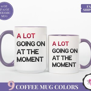 Puede incluir: Dos tazas de cer&aacute;mica blancas con asas y bordes morados. Las tazas tienen el texto "A LOT GOING ON AT THE MOMENT" en negro y rojo. Una taza es m&aacute;s grande que la otra. La imagen tambi&eacute;n incluye el texto "9 COFFEE MUG COLORS".