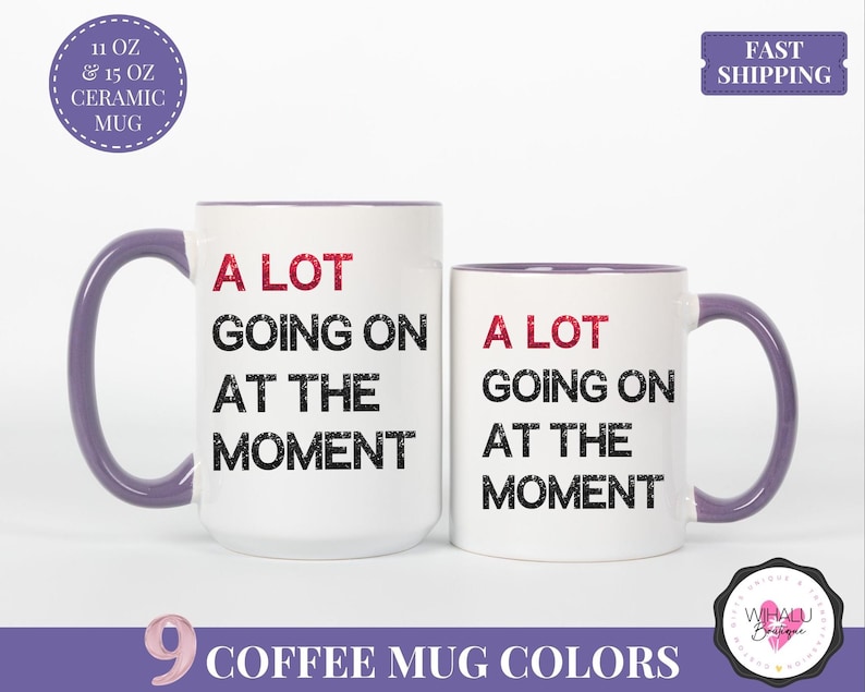 Puede incluir: Dos tazas de cer&aacute;mica blancas con asas y bordes morados. Las tazas tienen el texto "A LOT GOING ON AT THE MOMENT" en negro y rojo. Una taza es m&aacute;s grande que la otra. La imagen tambi&eacute;n incluye el texto "9 COFFEE MUG COLORS".