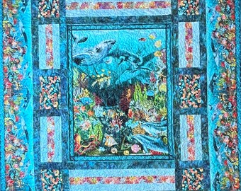 May include: A blue and green quilt with a large underwater scene in the center. The scene features a whale, fish, and coral. The quilt is surrounded by a border of smaller underwater scenes.