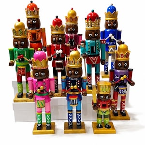 Puede incluir: Una colección de diez figuras de cascanueces de madera, cada una con una corona y pintada en colores vibrantes como rosa, azul, verde, rojo y naranja. Varias figuras sostienen pequeños tambores con baquetas, mientras otras llevan espadas.