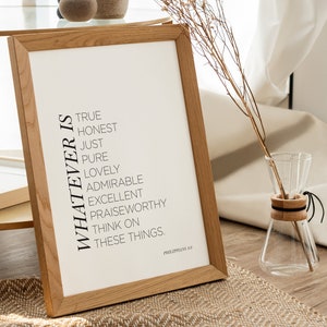 May include: A framed print with a white background and black text that reads "Whatever is true, honest, just, pure, lovely, admirable, excellent, praiseworthy, think on these things." The text is centered on the print and is followed by "Philippians 4:8". The print is in a wooden frame and is sitting on a table with a vase of dried flowers.