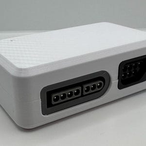 May include: A white rectangular electronic device with a textured top and black ports. The device has a USB port on the side and two sets of ports on the front. The ports are black and have multiple pin connectors.