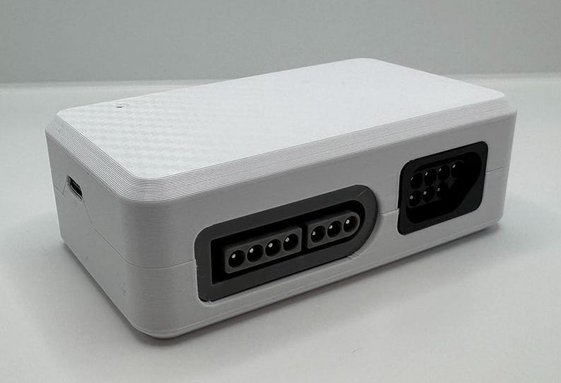 May include: A white rectangular electronic device with a textured top and black ports. The device has a USB port on the side and two sets of ports on the front. The ports are black and have multiple pin connectors.