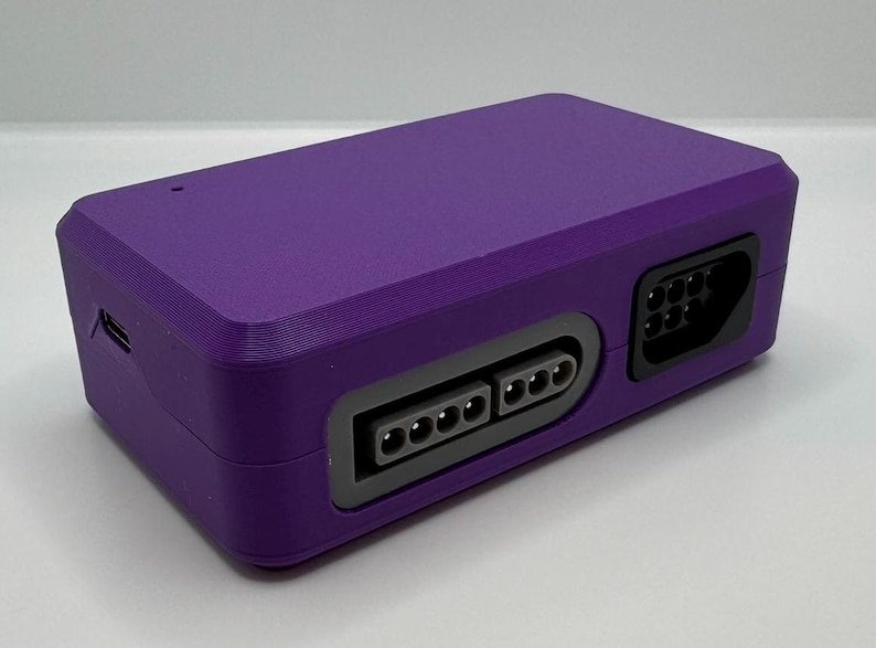 May include: A rectangular, purple electronic device with multiple ports. The device has a textured surface and a dark gray border around the ports. The ports include a USB port and several other connector ports.