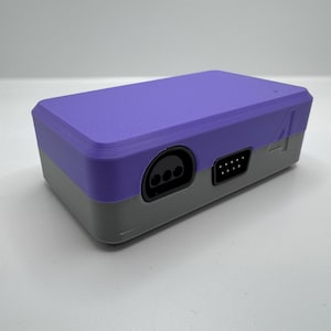 May include: A two-tone, purple and gray rectangular electronic device. The top is purple, and the bottom is gray. It has several ports on the front, including a circular port and a rectangular port. The number "4" is printed on the side.