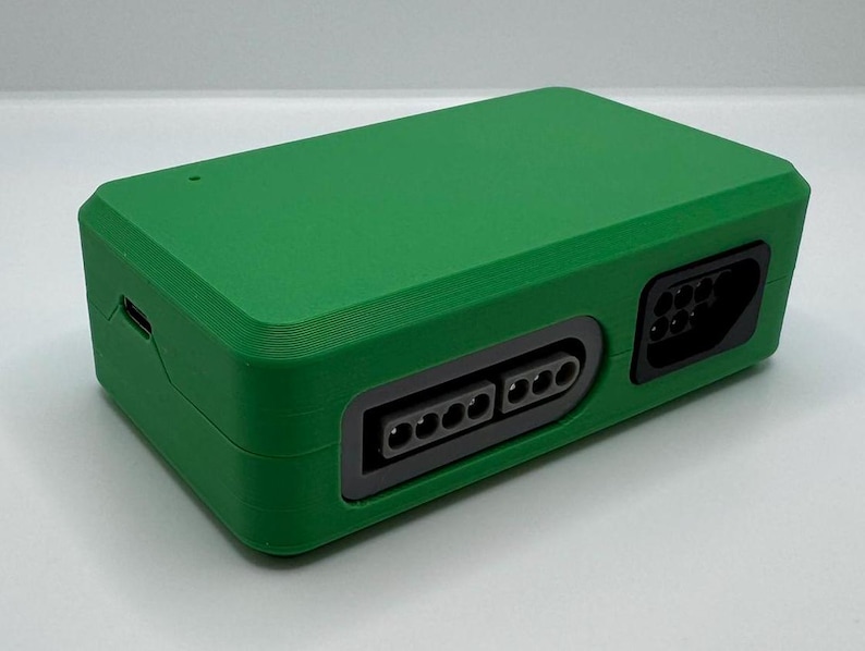 May include: A green rectangular electronic device with multiple ports. The device has a textured surface and a dark gray port on the side. The device has a small port on the side and a small light on the top.