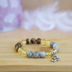 Può includere: Un braccialetto di perline con pietre di occhio di tigre, citrino e labradorite. Il braccialetto ha un ciondolo d'argento con il simbolo Om.