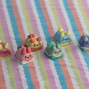 Può includere: Sei tasti per tastiera a forma di dinosauro colorati con facce carine. I tasti sono realizzati in argilla polimerica e sono dipinti in vari colori, tra cui rosa, giallo, blu, verde e viola. Ogni tasto ha un design diverso, con alcuni che presentano corna, punte e altre caratteristiche di tipo dinosauro.