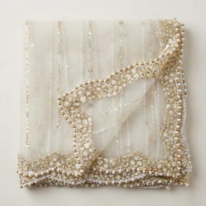 May include: Ivory sheer fabric with gold sequins and beaded trim. The fabric is folded, highlighting the intricate details of the embellishments. The border features a delicate pattern of sequins and small beads, adding a touch of elegance.