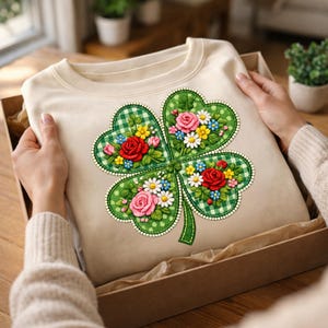 Peut inclure: Un sweat-shirt crème avec un motif de trèfle à quatre feuilles brodé. Le trèfle est vert avec un motif à carreaux et orné de fleurs rouges, roses, jaunes et blanches. Le sweat-shirt est présenté dans une boîte en carton.