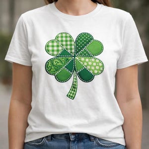 Peut inclure: T-shirt blanc avec un grand motif de trèfle à quatre feuilles vert. Le trèfle est composé de différents motifs verts, dont du vichy, des pois et des imprimés floraux, cousus ensemble. La tige est à carreaux verts et blancs.