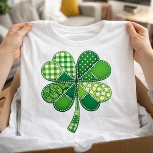 Peut inclure: T-shirt blanc avec un grand motif de trèfle à quatre feuilles vert. Le trèfle est composé de différents motifs verts, dont du vichy, des pois et des imprimés floraux, cousus ensemble avec du fil blanc. Thème festif de la Saint-Patrick.