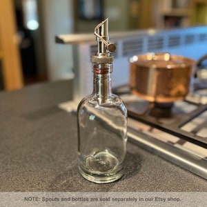 May include: A clear glass bottle with a silver metal spout. The bottle is empty and has a textured surface. NOTE: Spouts and bottles are sold separately in our Etsy shop.