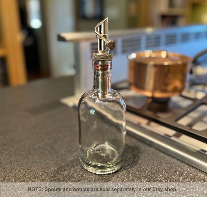 May include: A clear glass bottle with a silver metal spout. The bottle is empty and has a textured surface. NOTE: Spouts and bottles are sold separately in our Etsy shop.