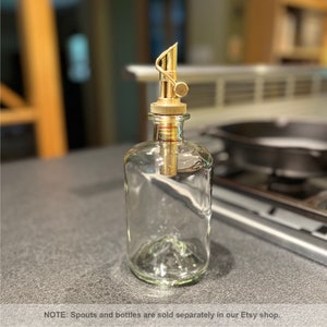 May include: A clear glass bottle with a gold metal spout and a knob. The bottle is on a gray countertop.