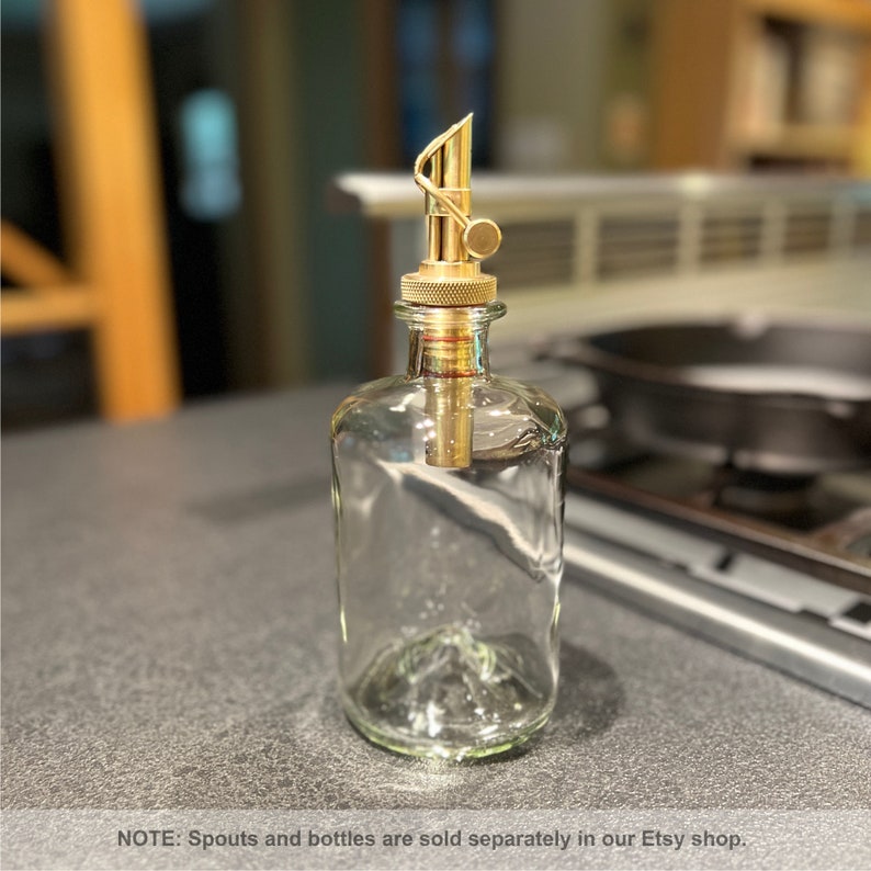 May include: A clear glass bottle with a gold metal spout and a knob. The bottle is on a gray countertop.