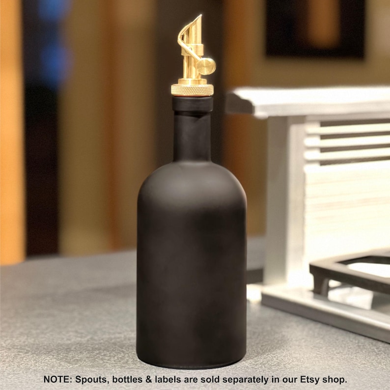 May include: A black glass bottle with a gold metal spout shaped like a treble clef. The bottle is sitting on a counter top.